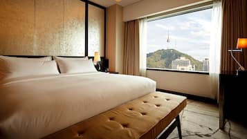 A hotel room with a large bed, a bench, a nightstand, a lamp, and a view of a cityscape through a large window.
