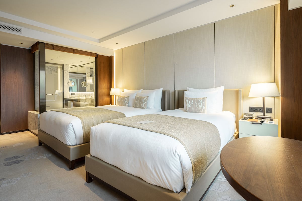 A hotel room with two beds, a large mirror, bedside tables with lamps, and a wooden headboard.