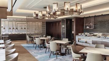 A modern hotel lobby with a marble reception desk, multiple dining tables, and contemporary lighting fixtures.