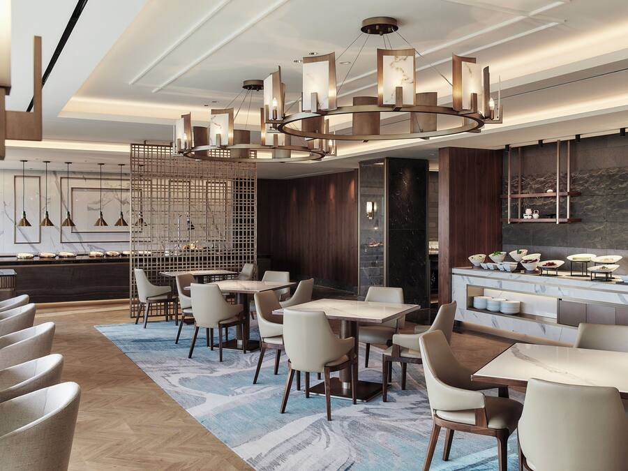 A modern hotel lobby with a marble reception desk, multiple dining tables, and contemporary lighting fixtures.