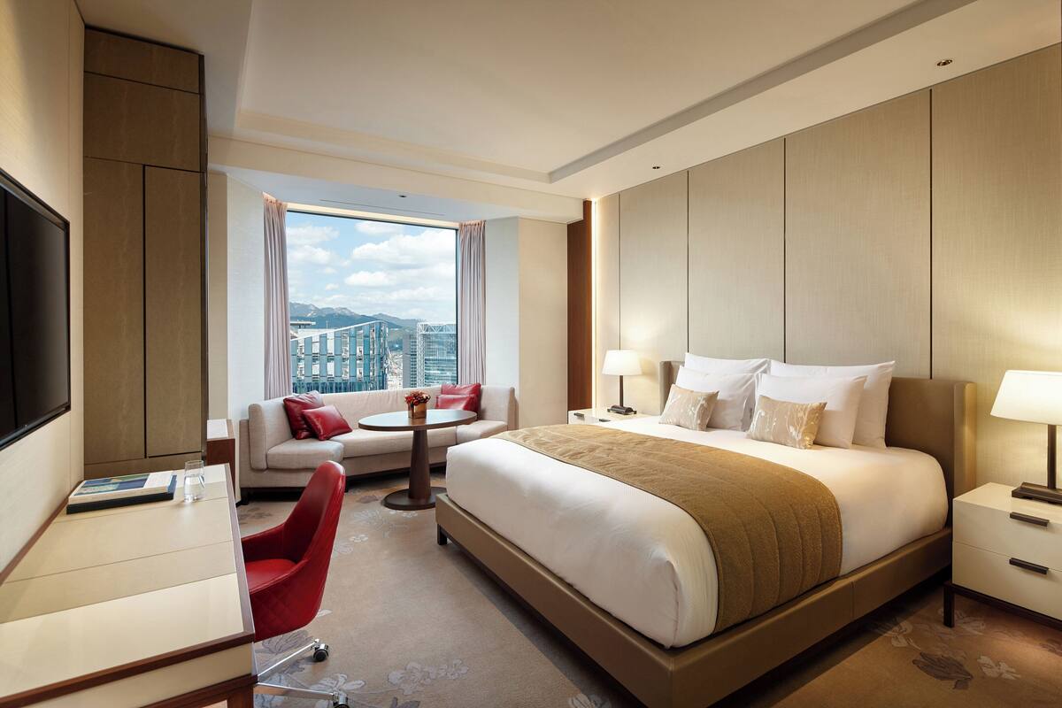 A modern hotel room with a large bed, a sofa, a desk, and a TV.