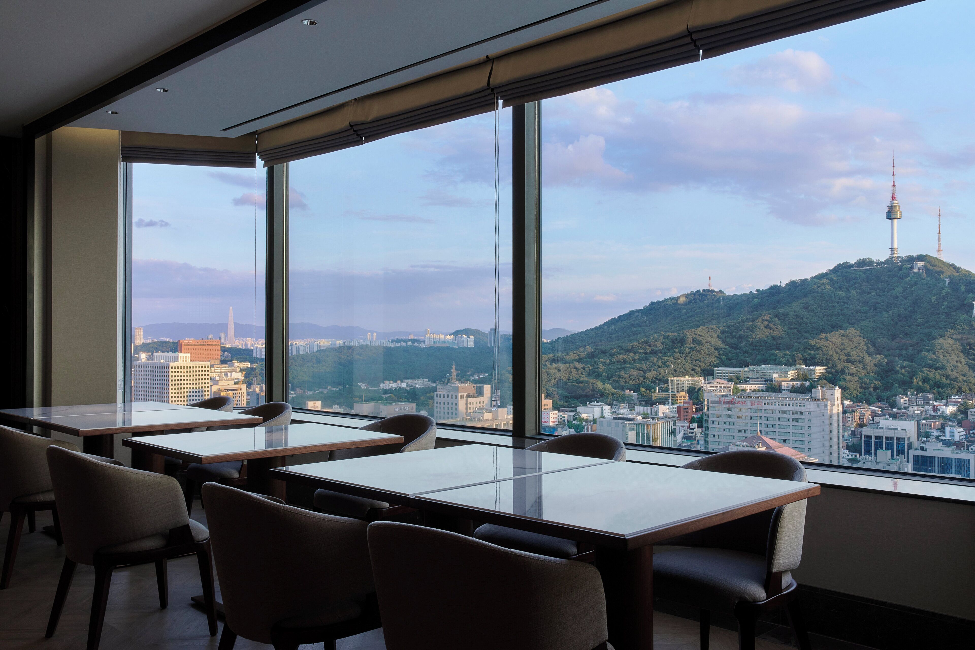 A modern hotel room with large windows offering a city view, including a prominent tower.