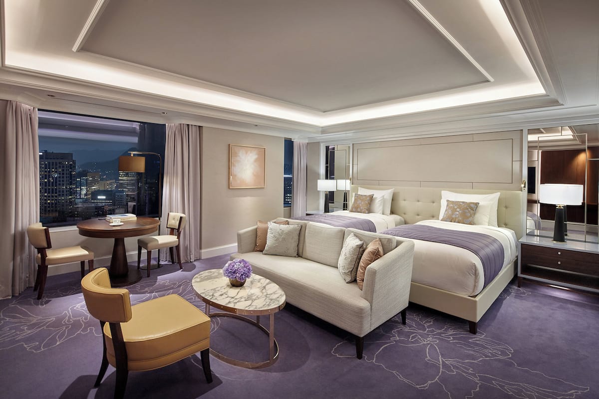 A hotel room with a large bed, a sofa, a round table, and a view of the city at night.