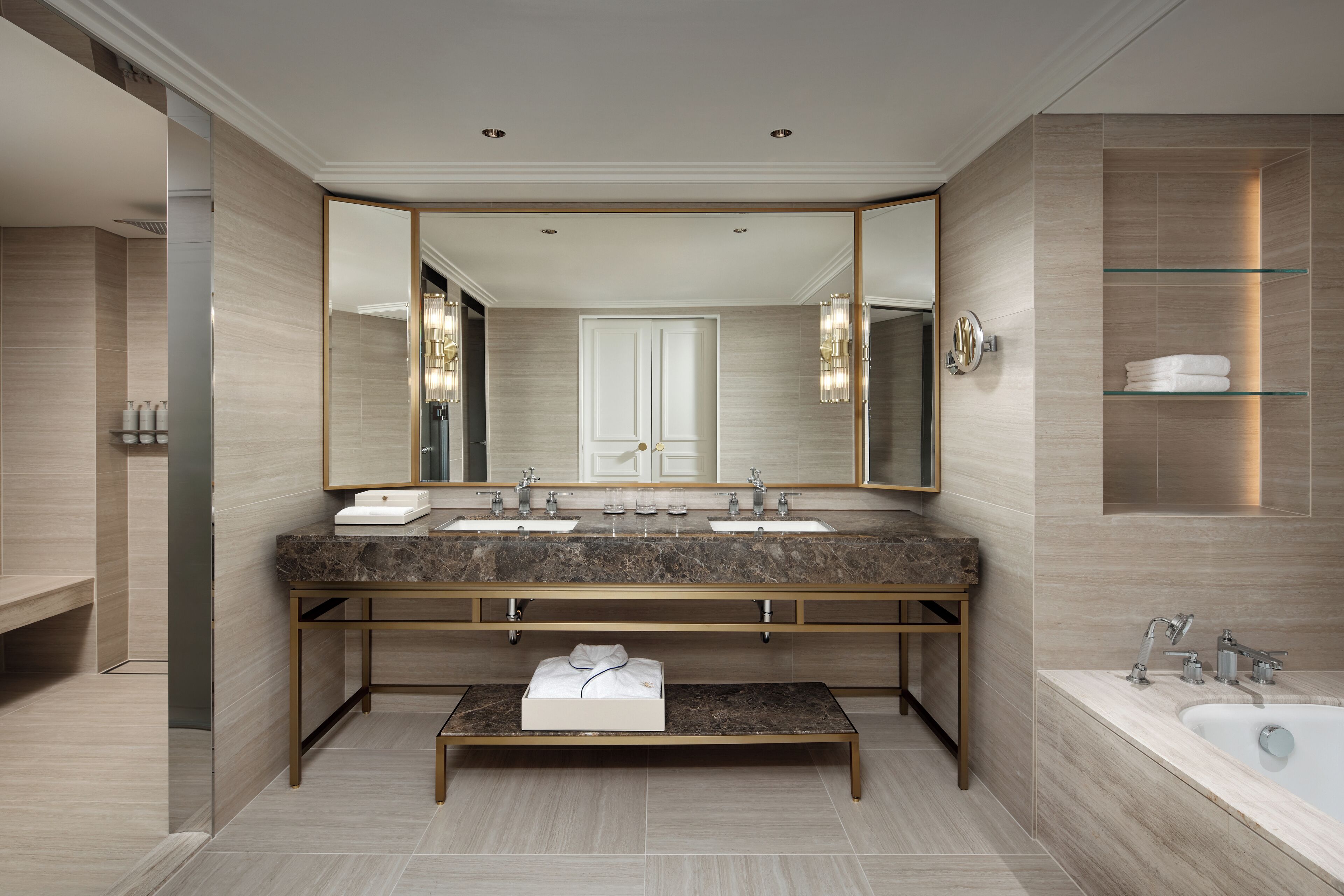 A modern bathroom with a large mirror, dual sinks, a bench, and a bathtub.