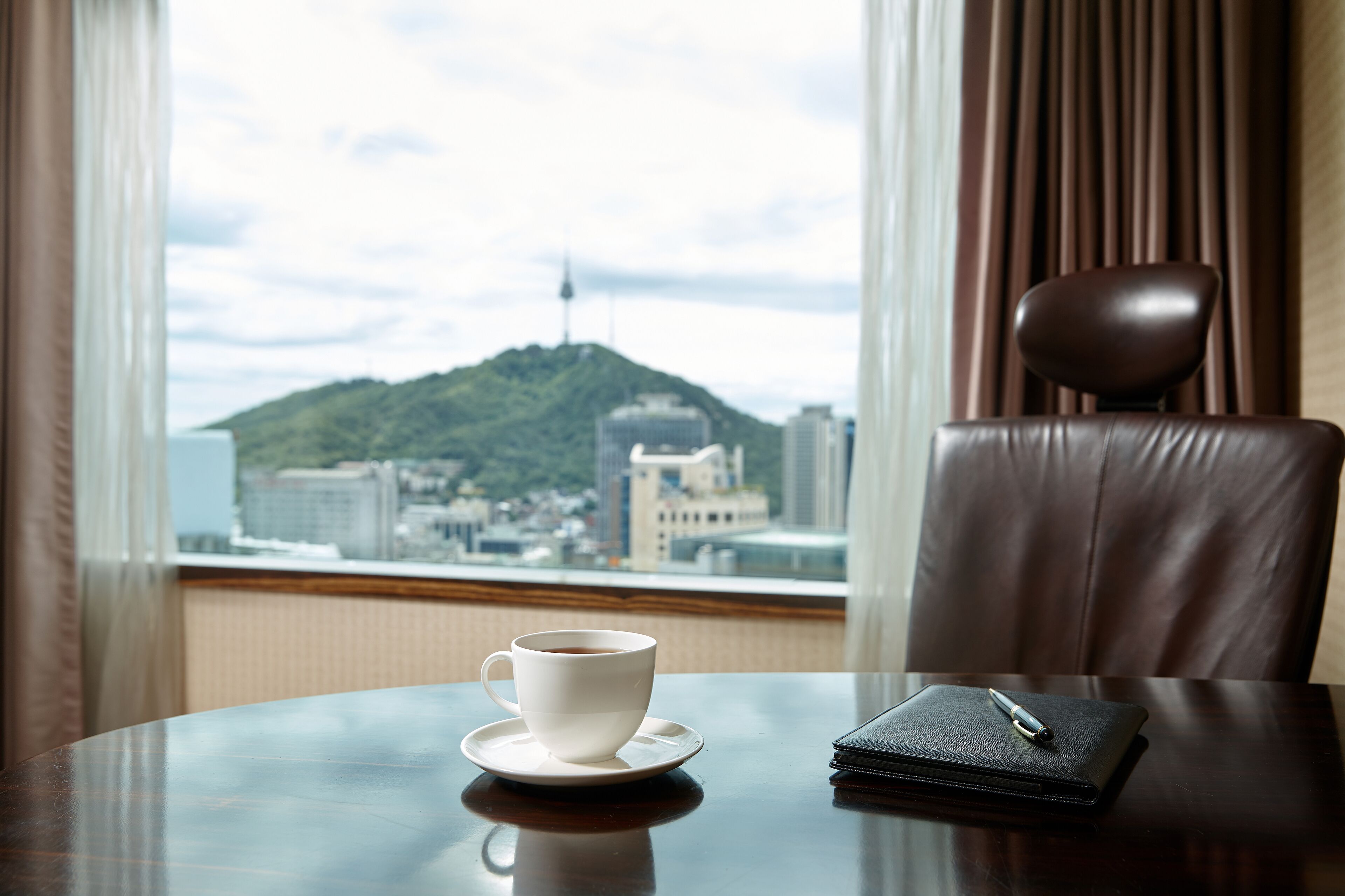 A hotel room with a round table, a cup of coffee, a wallet, and a chair.