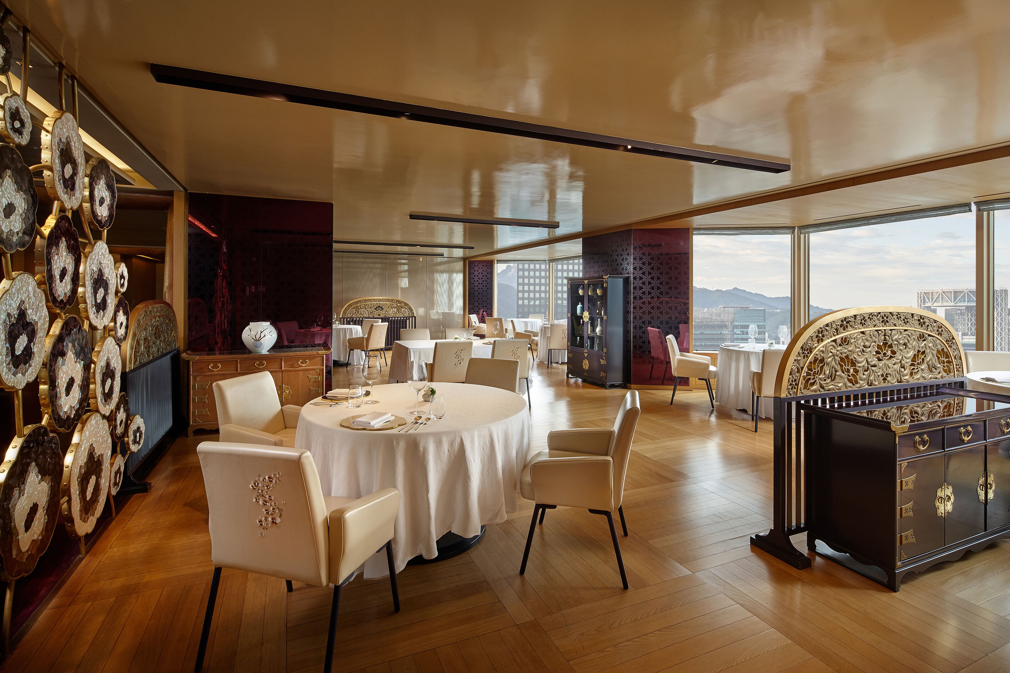 A spacious dining area with round tables, white chairs, and a decorative cabinet.