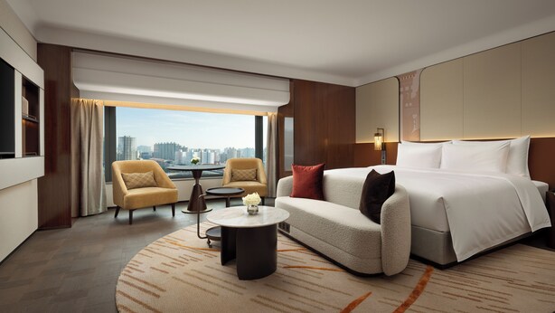 A modern hotel room with a large bed, a sofa, a small round table, two armchairs, a view of the city, and a large window. - The Kunlun Hua Ting Hotel & Towers,Shanghai (Shanghai)