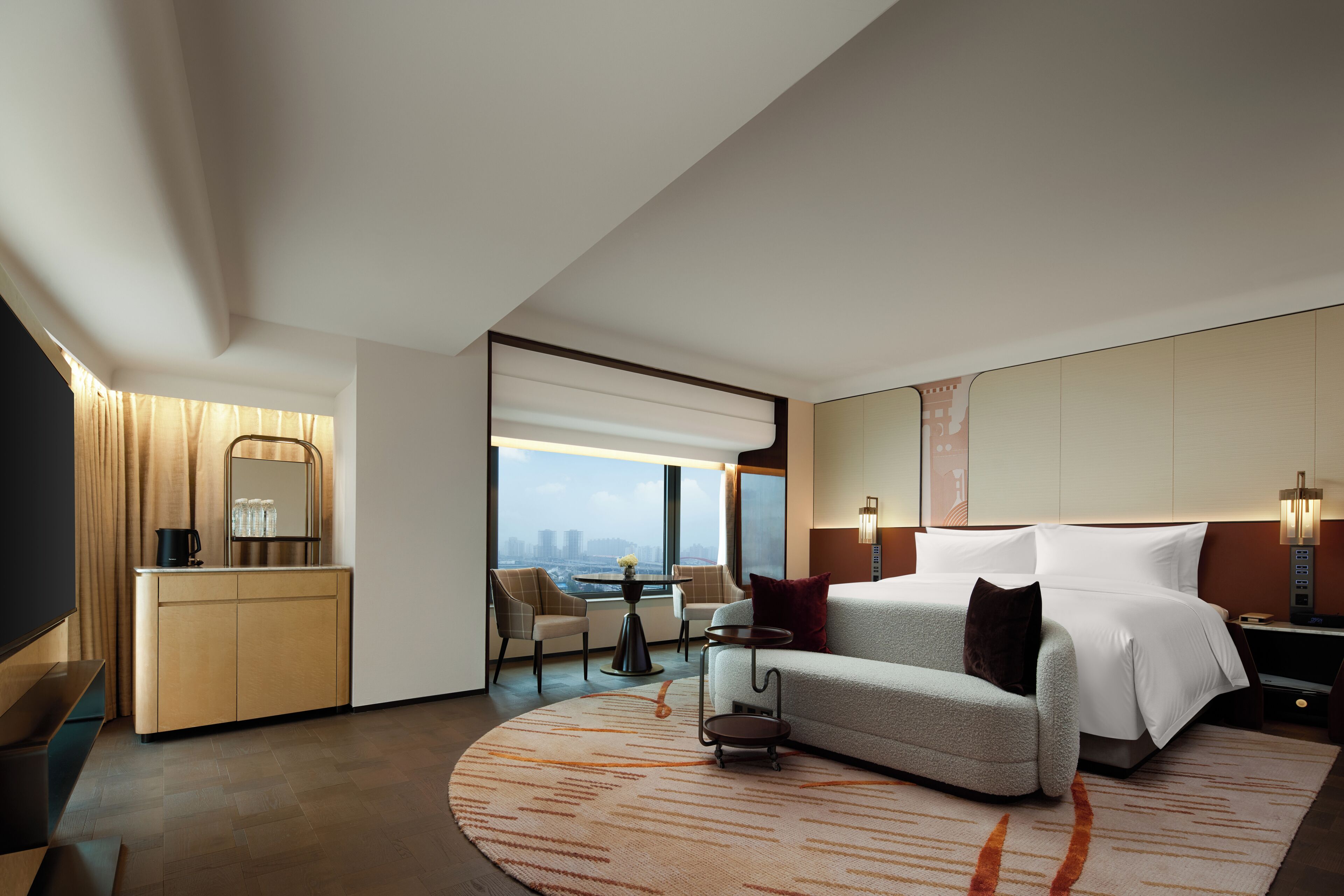 A modern hotel room with a bed, sofa, and a dining area with a table and chairs.