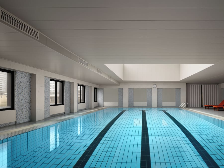 An indoor swimming pool with a skylight, tiled walls, and red lounge chairs.
