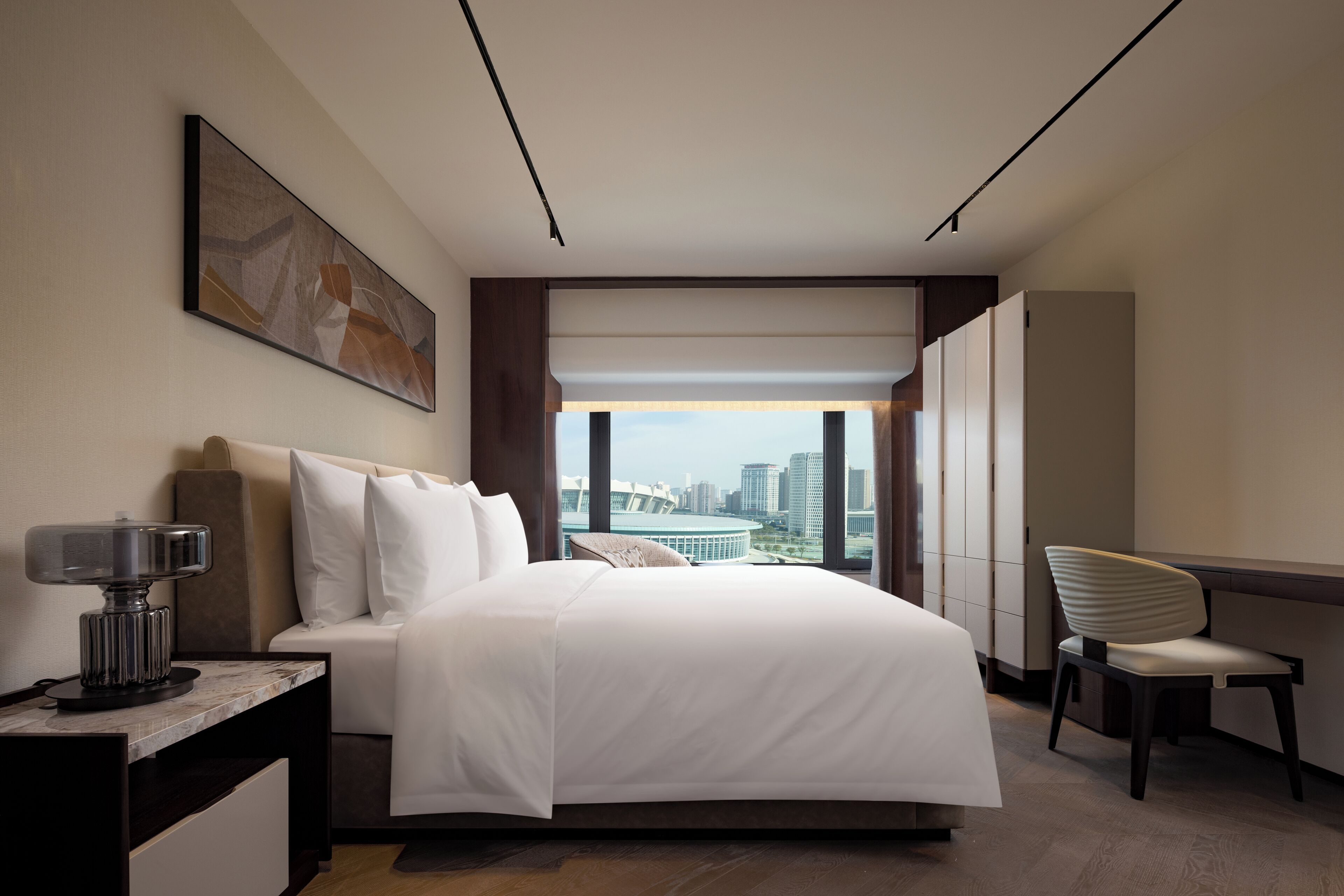 Ein modernes Hotelzimmer mit einem großen Bett, einem Schreibtisch, einem Stuhl und Blick auf die Stadt.