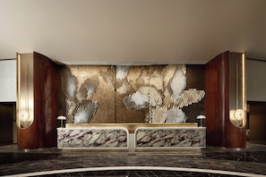 A reception desk with a marble top, a patterned wall, and two wall-mounted lamps. - The Kunlun Hua Ting Hotel & Towers,Shanghai (Shanghai)
