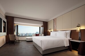 A modern hotel room with a large bed, a seating area with a chair, a side table, and a view of the city.