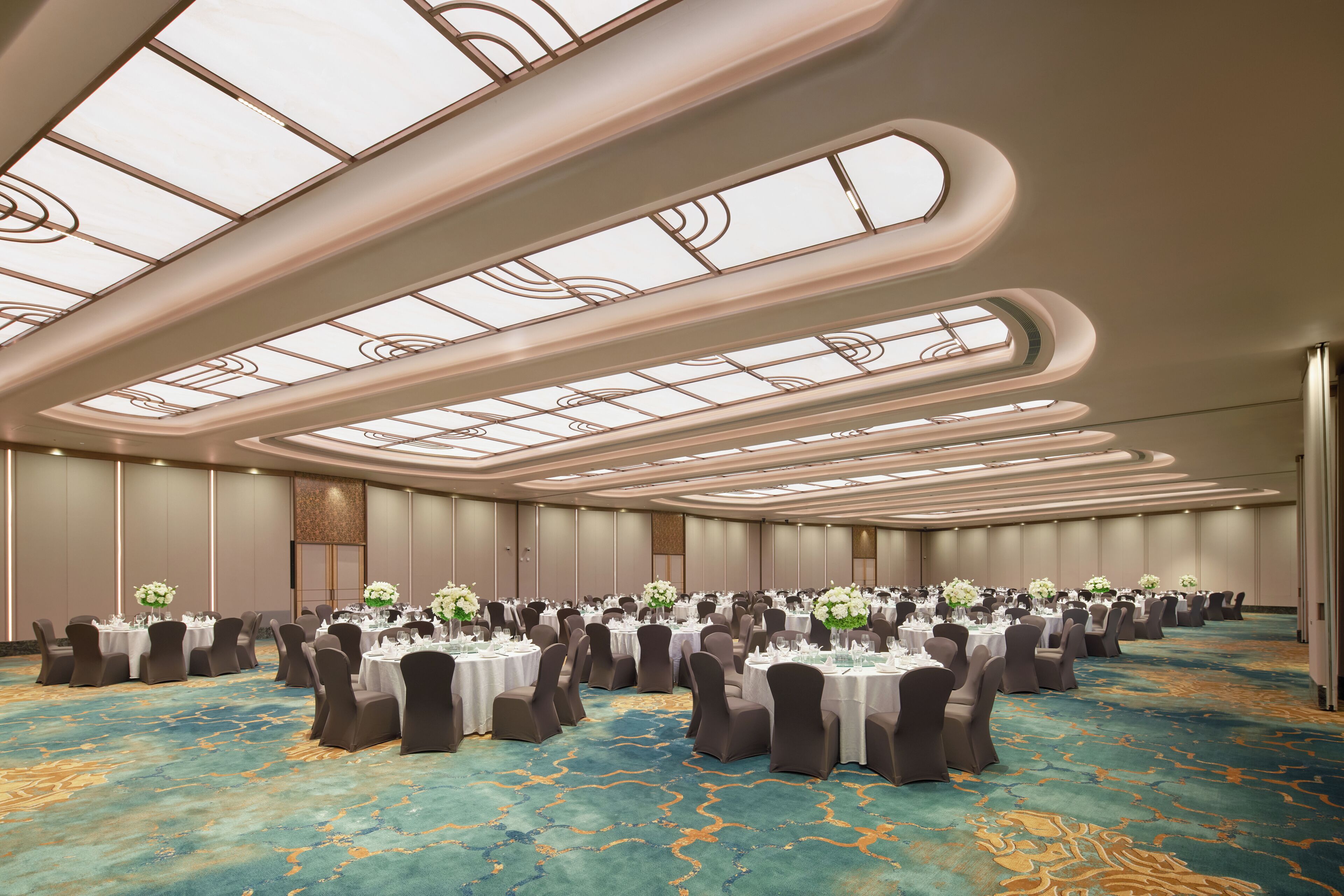 Un amplio salón de conferencias con mesas redondas, sillas y centros de mesa florales.