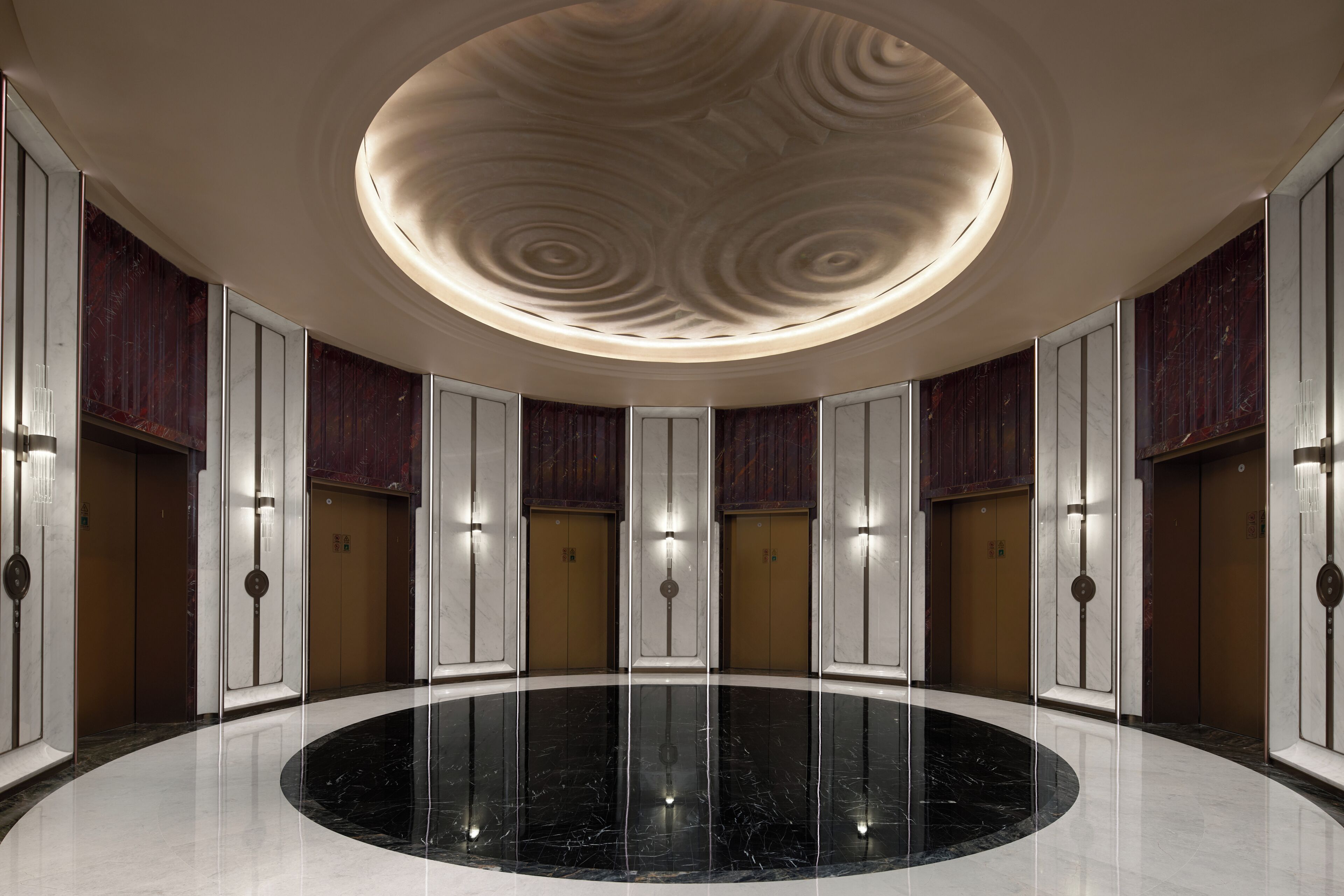A circular lobby with a polished marble floor, a central light fixture, and elevators.