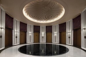 A circular lobby with a polished marble floor, a central light fixture, and elevators.