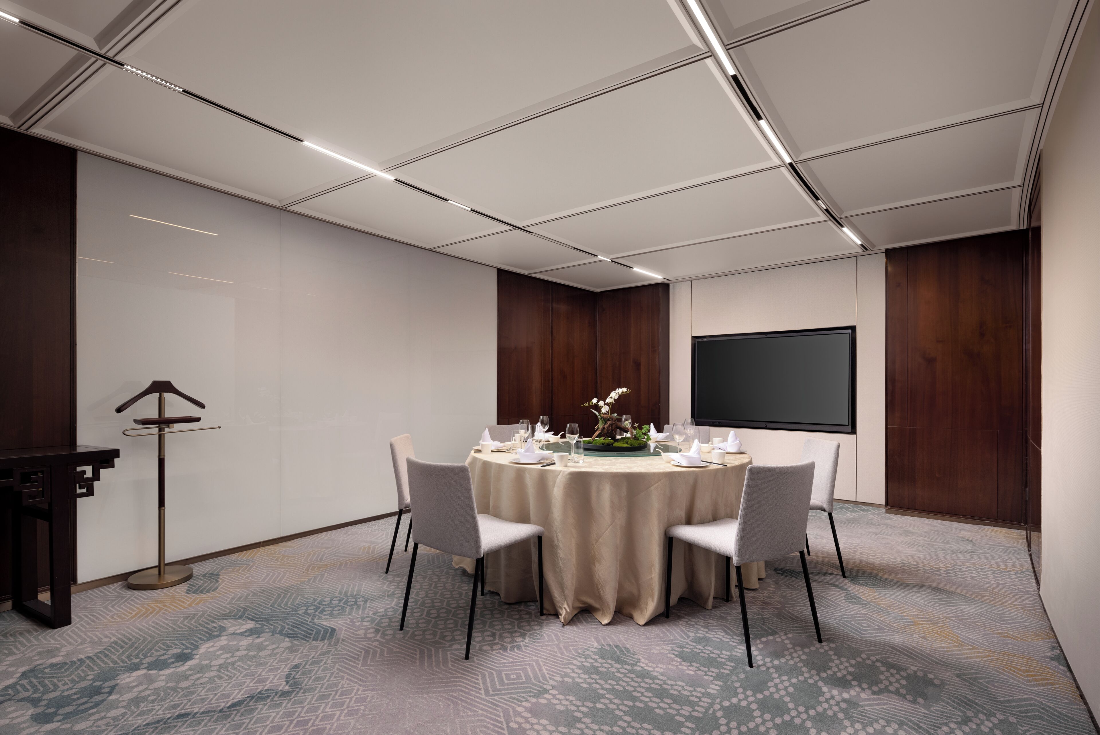A conference room with a round table, four chairs, a projector screen, and a decorative plant.