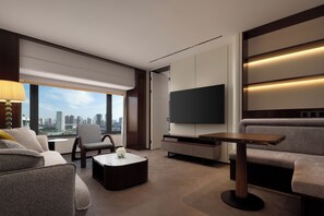 A modern living room with a sofa, armchair, coffee table, TV, and city view.