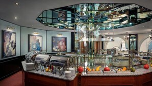 Un moderno vestíbulo de hotel con una escalera de cristal, zona de bufé y obras de arte en las paredes.
