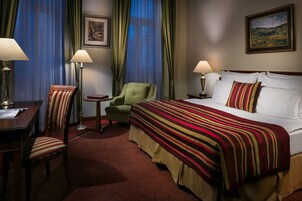 Una camera d'albergo con un letto, due sedie, una scrivania e una lampada.