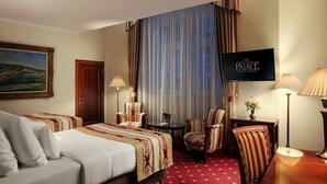Habitación de hotel con una cama, dos sillones, un escritorio, un televisor y un cuadro en la pared.