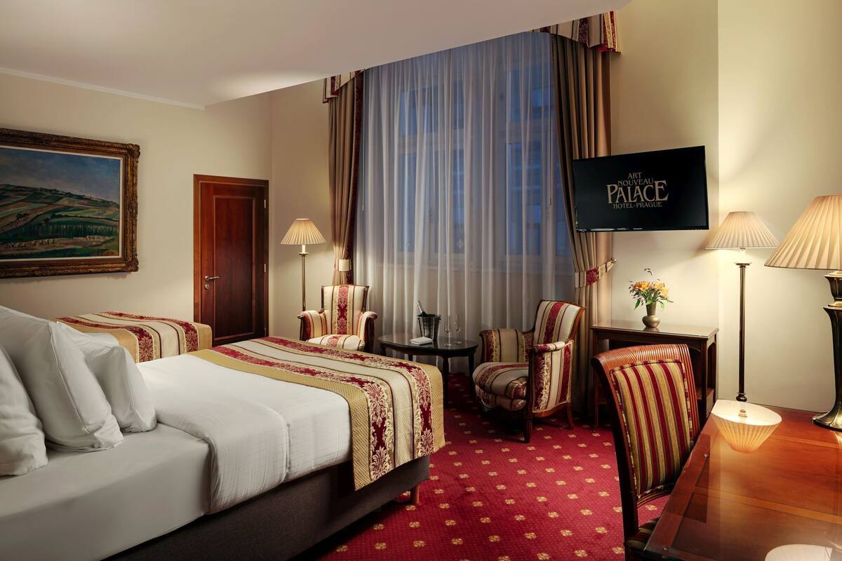Een hotelkamer met een bed, twee fauteuils, een bureau, een televisie en een schilderij aan de muur.