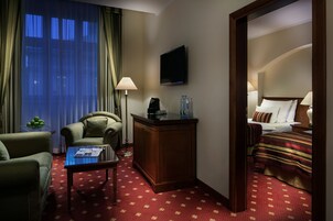 Quarto de hotel com cama, escrivaninha, cadeira, televisão e janela com cortinas.
