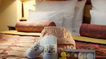 A hotel room with a bed, pillows, a lamp, slippers, and a toiletries box.