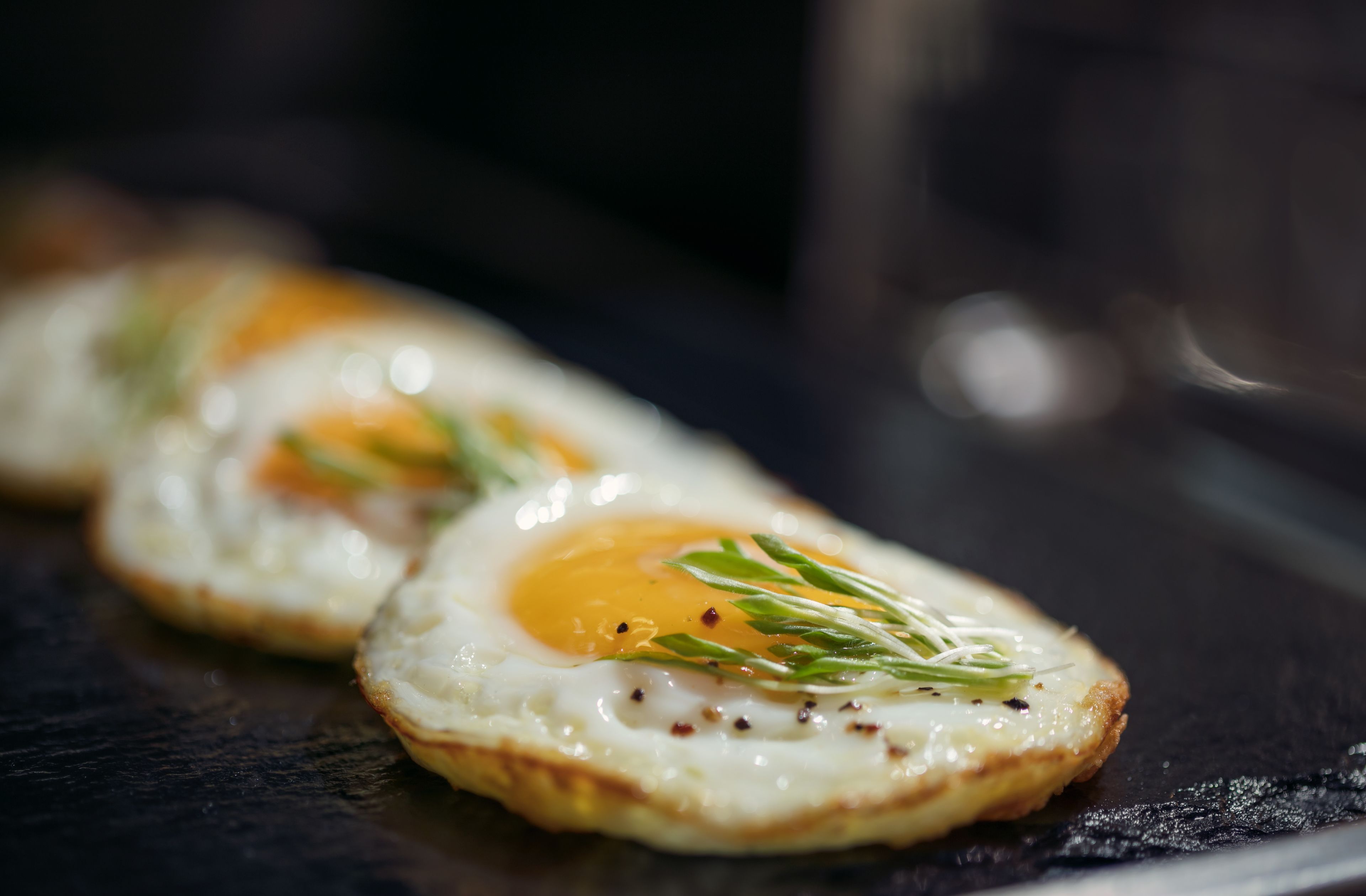 A close-up of two fried eggs garnished with herbs on a dark surface.