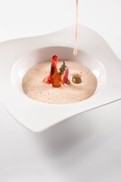 Un piatto quadrato bianco con una zuppa cremosa e un guarnello di carne.