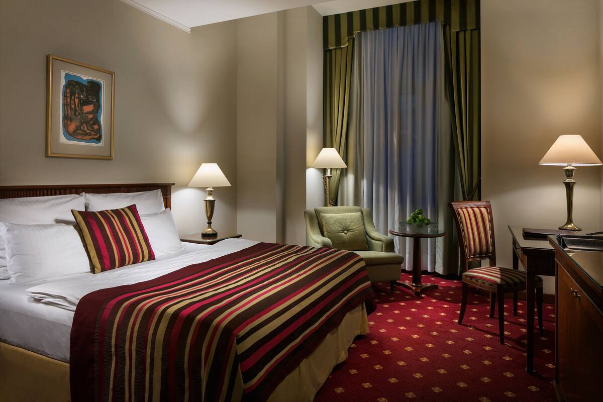 Een hotelkamer met een groot bed, twee stoelen, een tafeltje en een bureau.