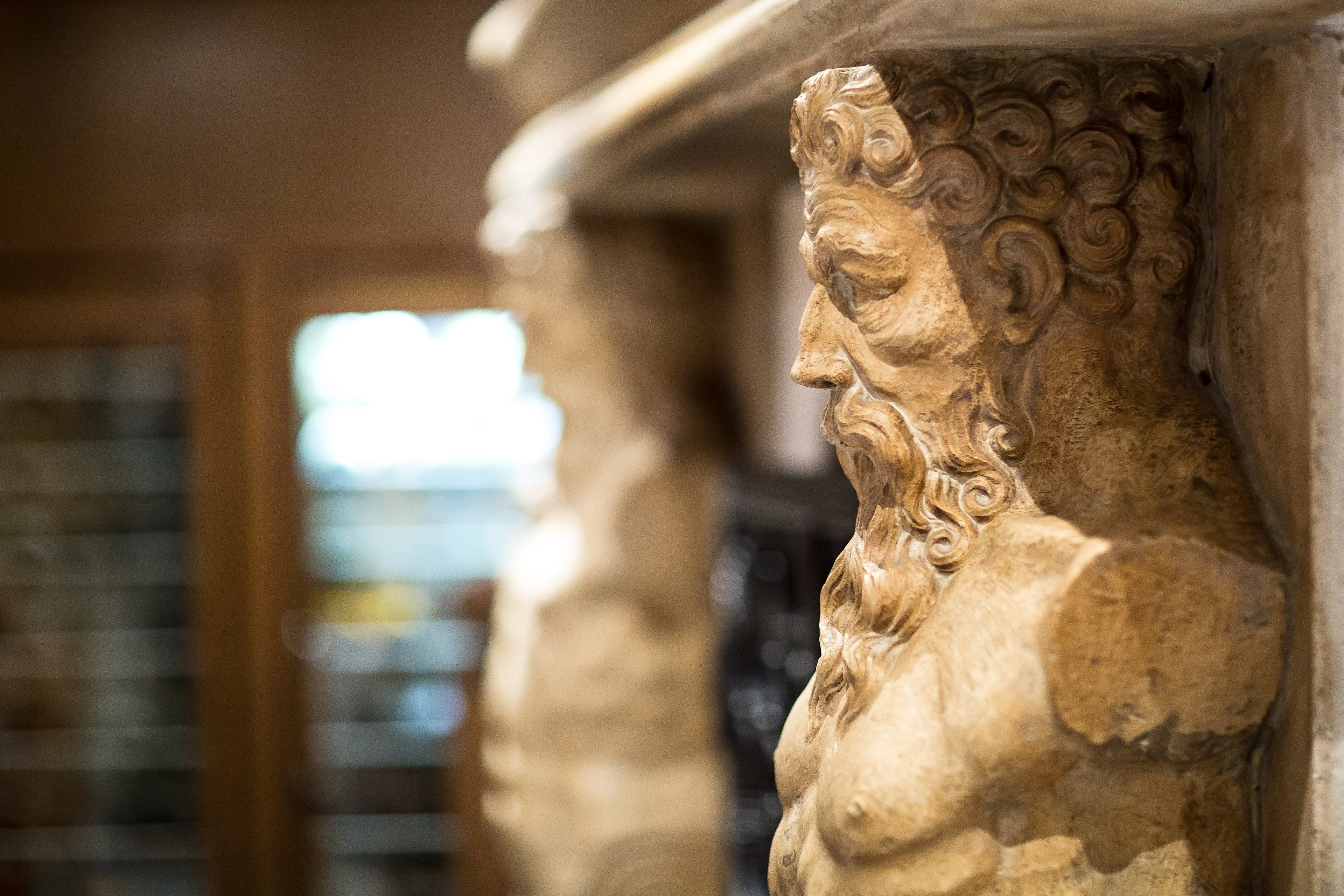 Ein Detailaufnahme einer Steinsäule mit aufwendigen Schnitzereien, vermutlich Teil der Architektur eines historischen Gebäudes.