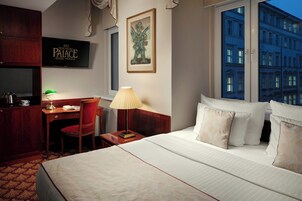 Una camera d'albergo con un letto, una scrivania, una sedia, una lampada e un quadro appeso al muro.