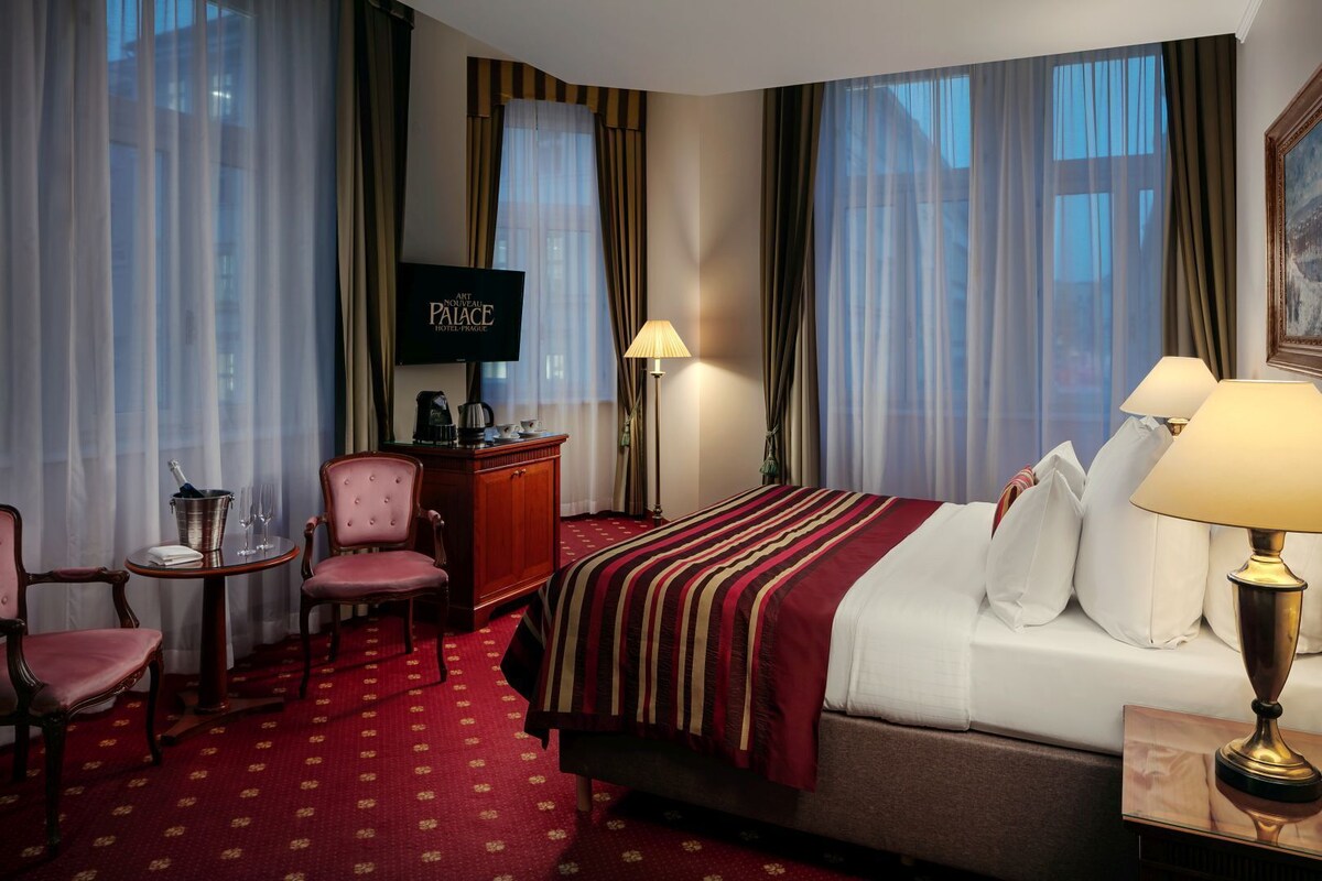 Habitación de hotel con cama, escritorio, silla, televisión y ventana con cortinas.