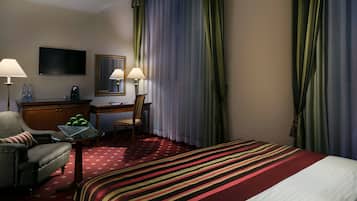 A hotel room with a bed, a desk, a chair, a TV, and a lamp.
