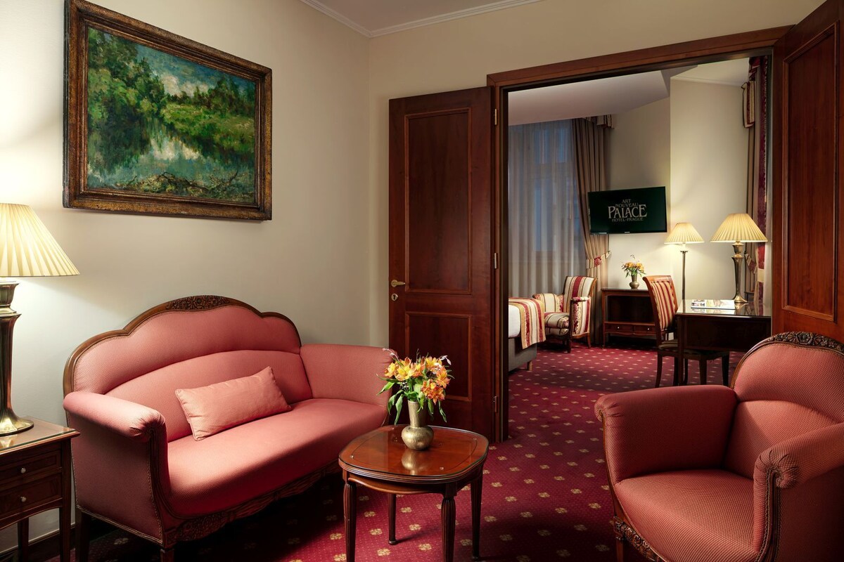 Habitación de hotel con un sofá rojo, una mesita con un jarrón y un cuadro en la pared.