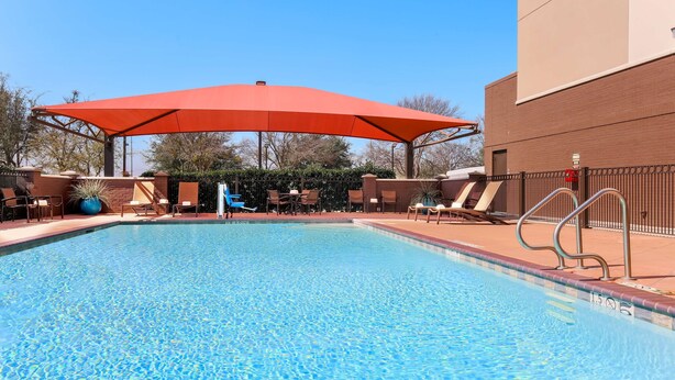 A swimming pool with a red canopy, lounge chairs, and a brick building in the background.
