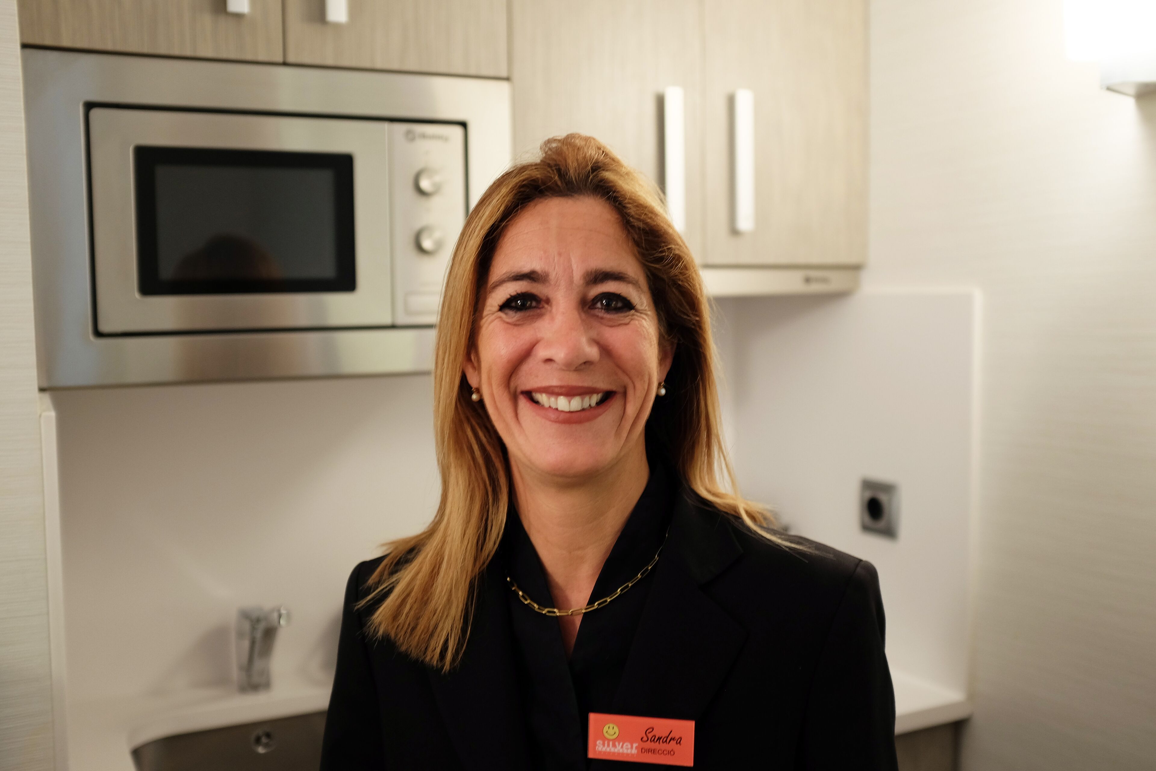 A person standing in a kitchen with stainless steel appliances, a sink, and light-colored cabinets.