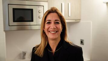 A person standing in a kitchen with stainless steel appliances, a sink, and light-colored cabinets.