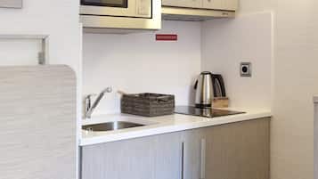 Una cucina compatta con lavandino in acciaio inossidabile, bollitore e forno a microonde sopra il piano di lavoro.