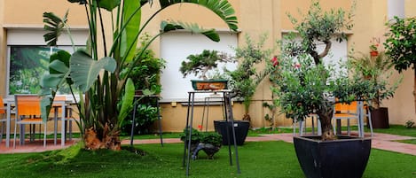 A courtyard with a small garden, outdoor seating, and a building with a beige wall and white shutters.