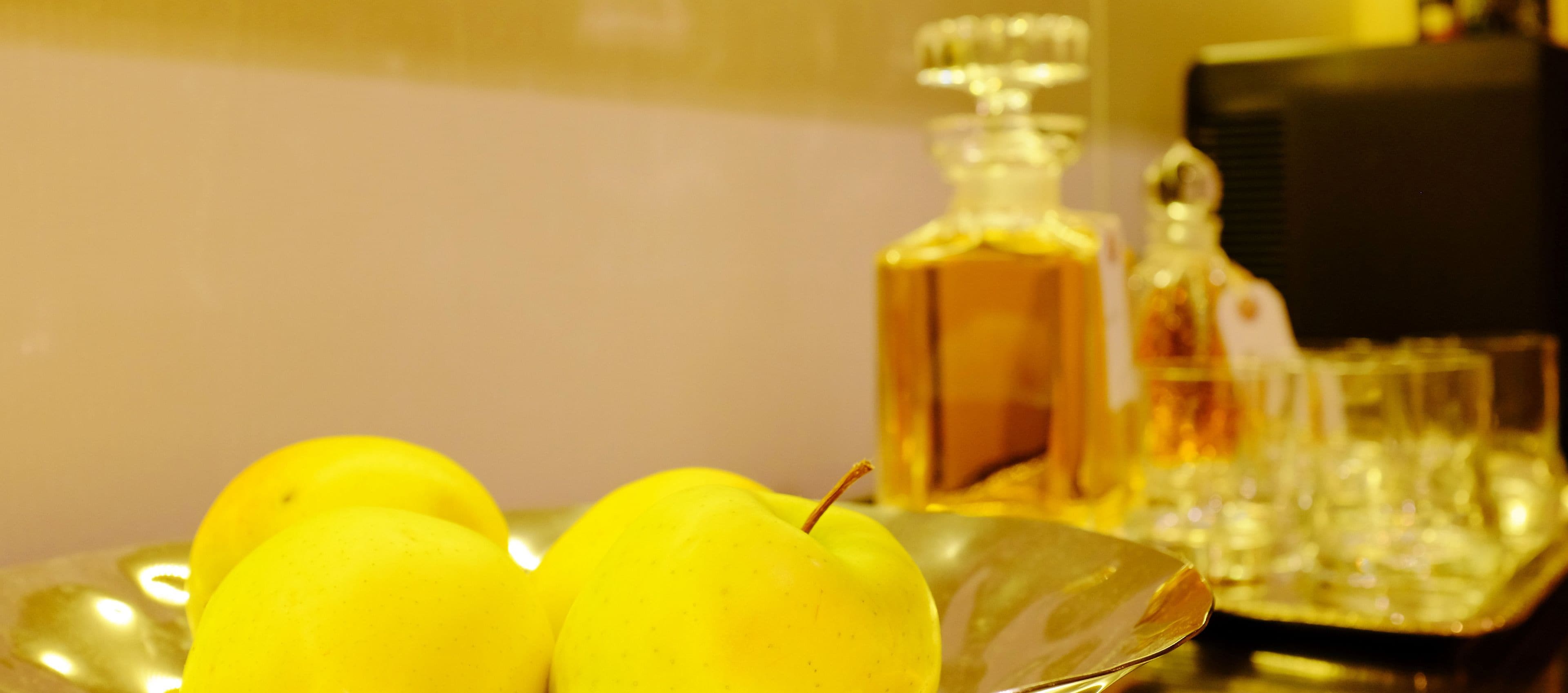 A close-up of a metal tray with three yellow lemons and a glass bottle with a label.