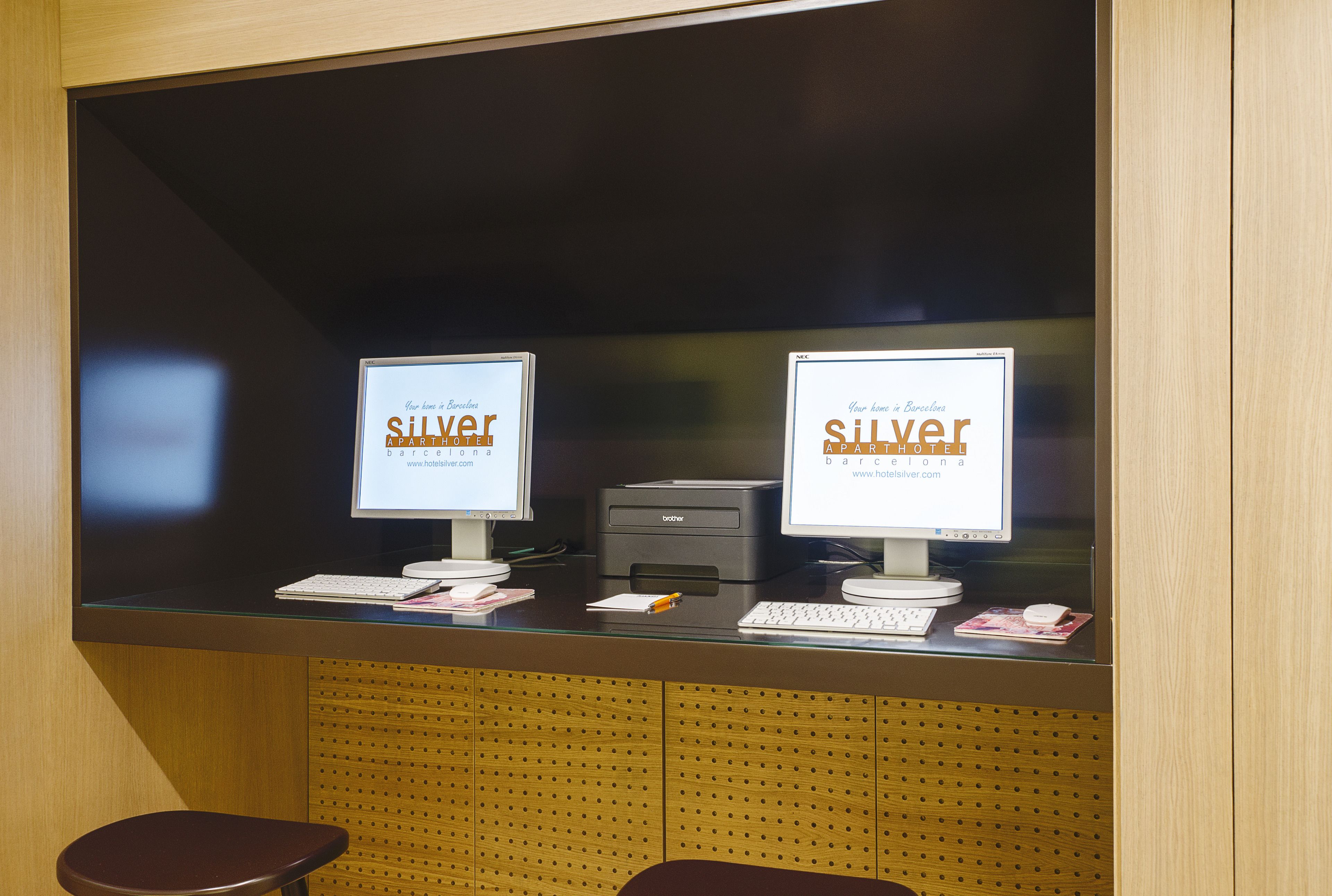 Two computer monitors with the text "Silver Hotel" on them, placed on a counter with a keyboard and a printer.