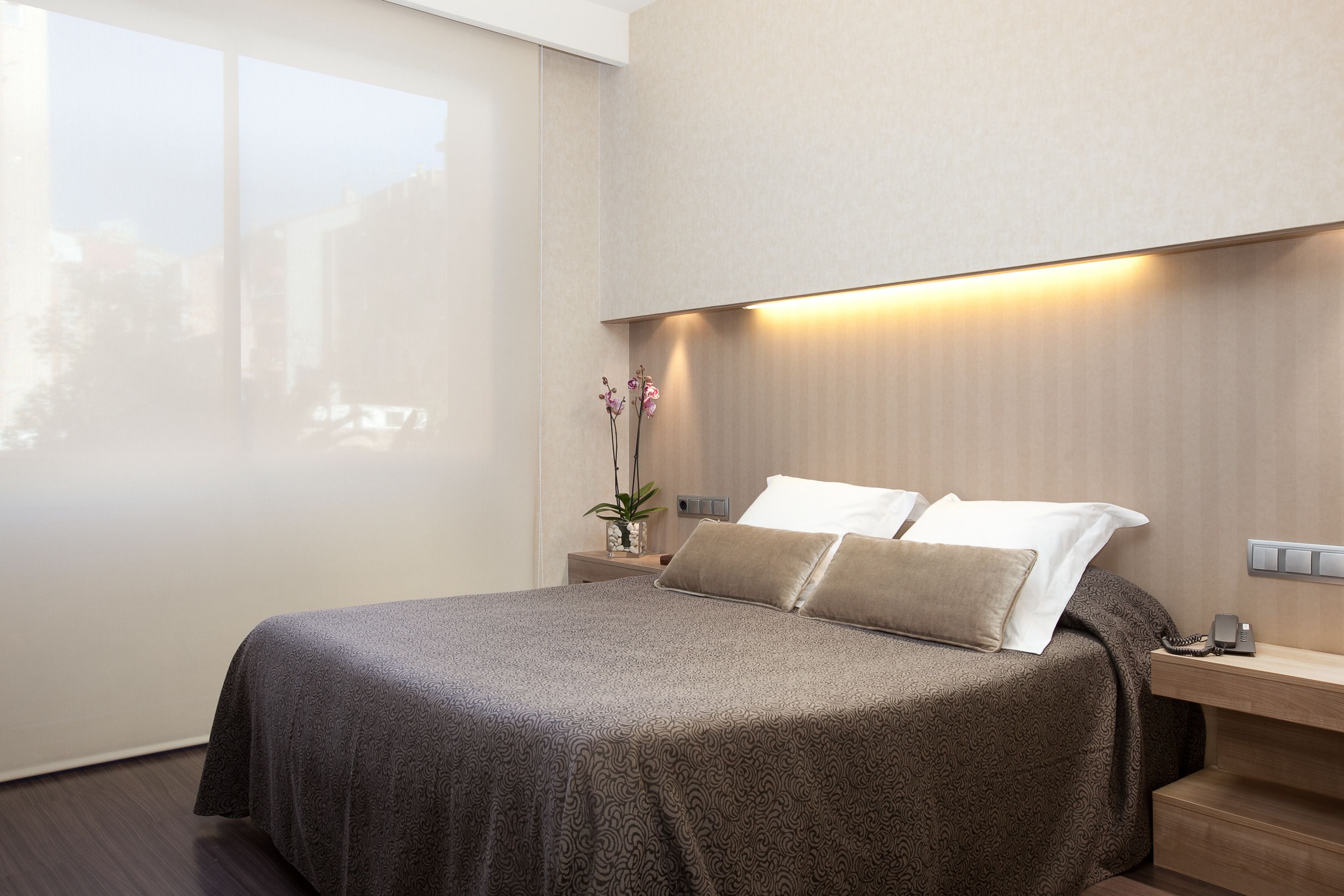 A modern hotel room with a large bed, a bedside table with a lamp, and a view of the outdoors.