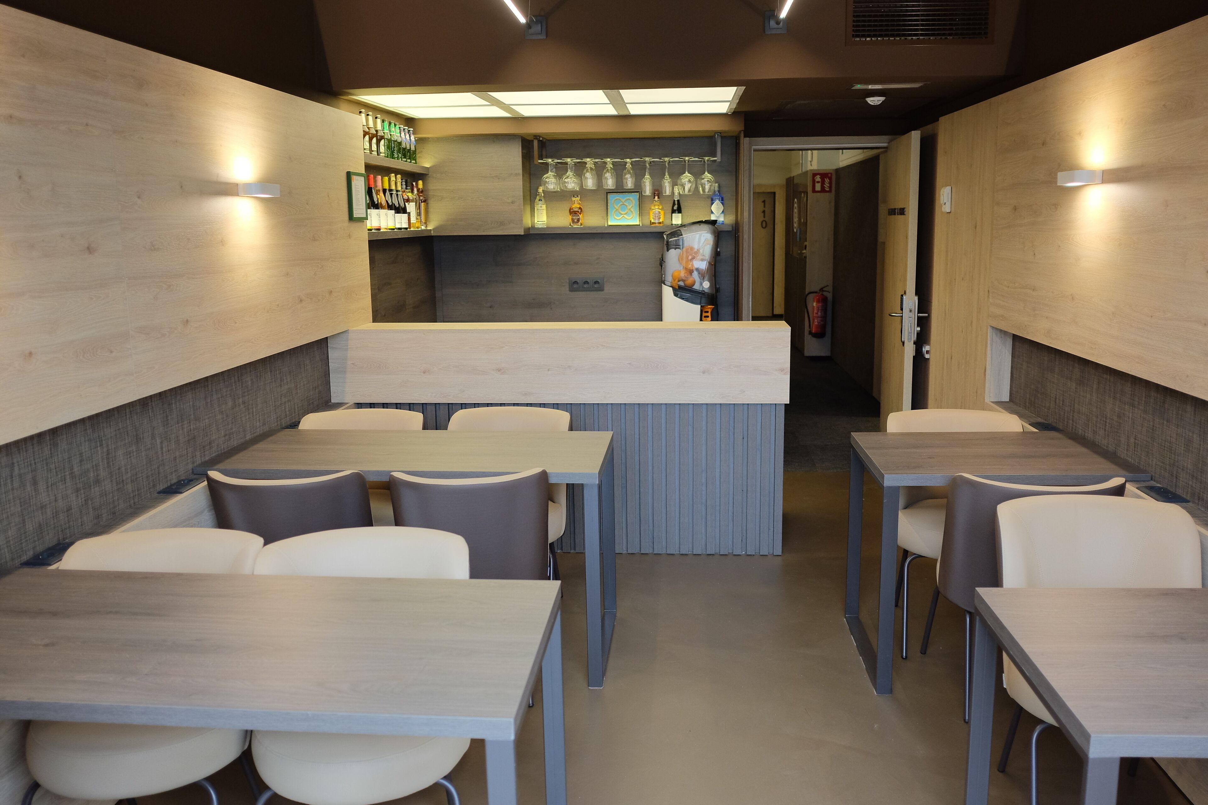 A modern restaurant with wooden walls, a bar area, and multiple seating tables and chairs.