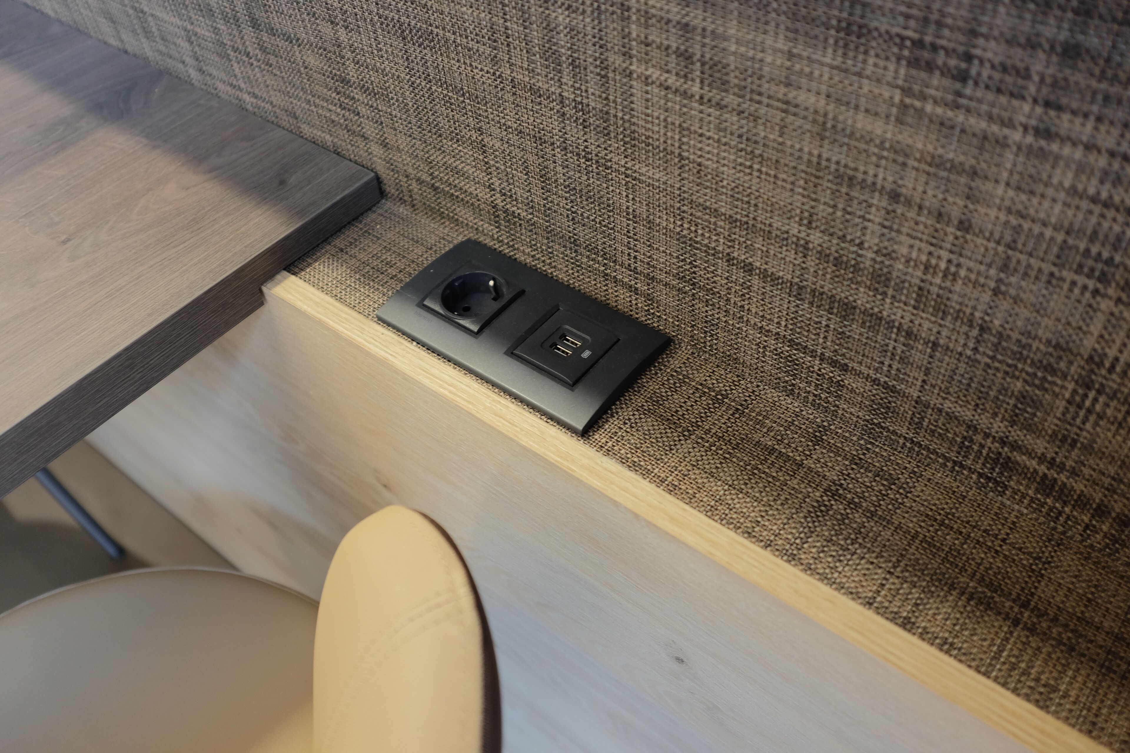 A corner of a room with a wooden table, a cushioned chair, and a built-in electrical outlet with a USB port.