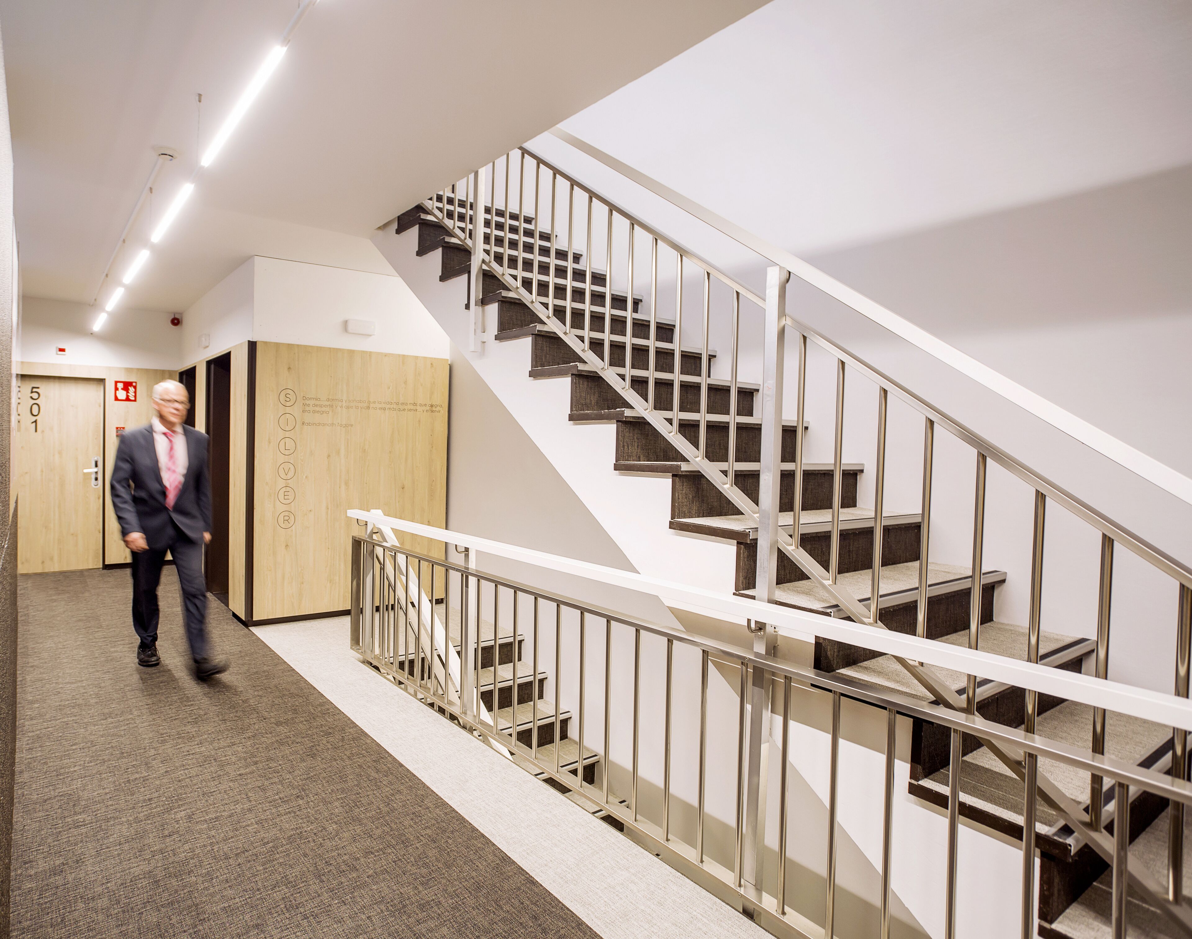 A modern interior with a staircase, a wooden door labeled "501", and a person walking.