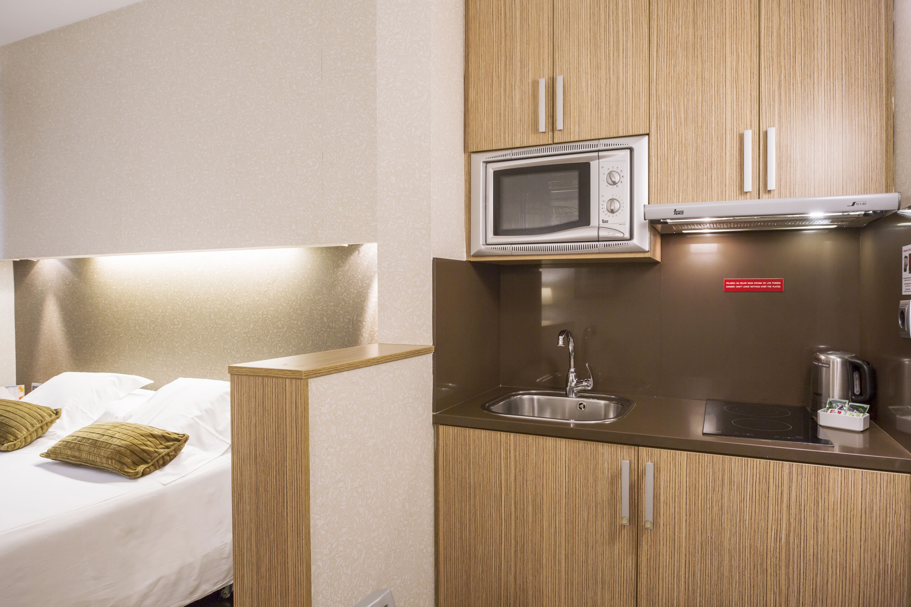 A compact hotel room with a kitchenette including a microwave, sink, and kettle.