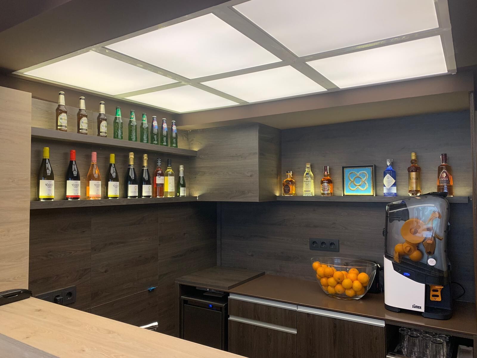 Eine moderne Küche mit Holzschränken, einem integrierten Weinkühlschrank, einer Kaffeemaschine und einer Schale Orangen auf der Arbeitsfläche.