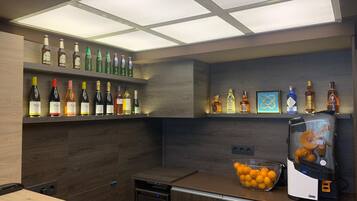 Une cuisine moderne avec des meubles en bois, un meuble-bar intégré, une machine à café et un saladier rempli d’oranges posé sur le plan de travail.