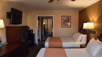 A hotel room with two beds, a TV, a desk, and a ceiling fan.